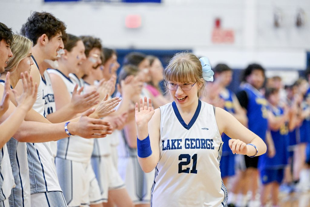 A smiling girl in a white and blue basketball jersey high-fiving a line of students in matching basketball uniforms.