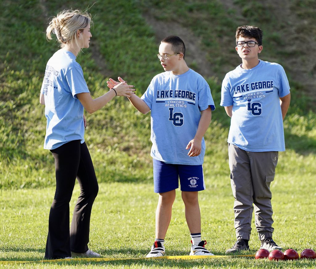 Three students standing in Lake George athletic shirts with bocce balls on the ground