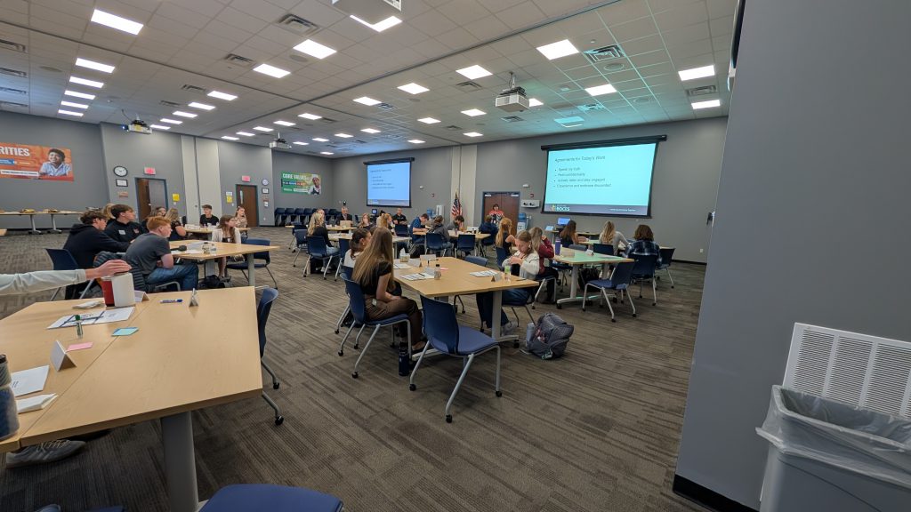 many students in a large room with projectors sitting at desks