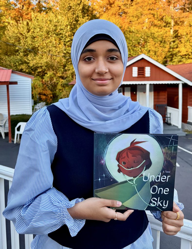 Student holding book with trees in the background