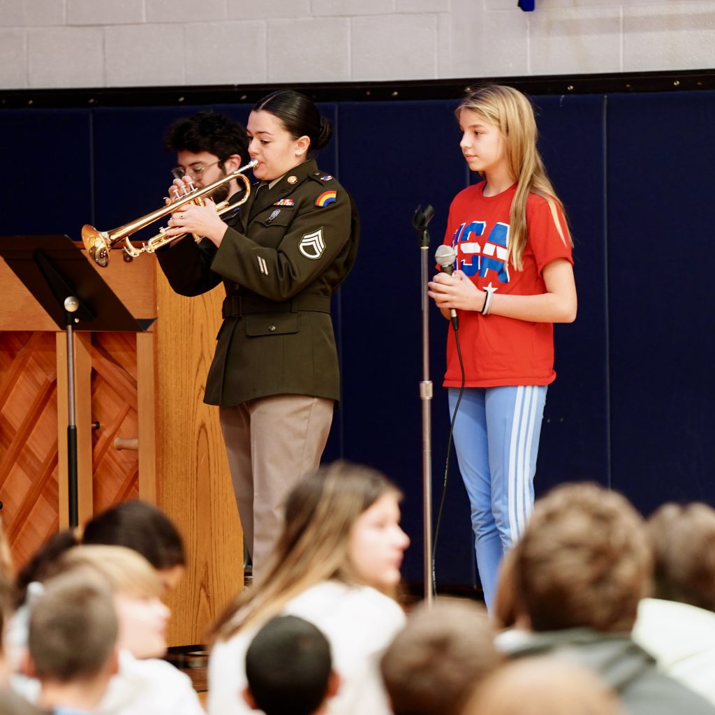 teacher in a military uniform playing a trumpet while student stands next to her
