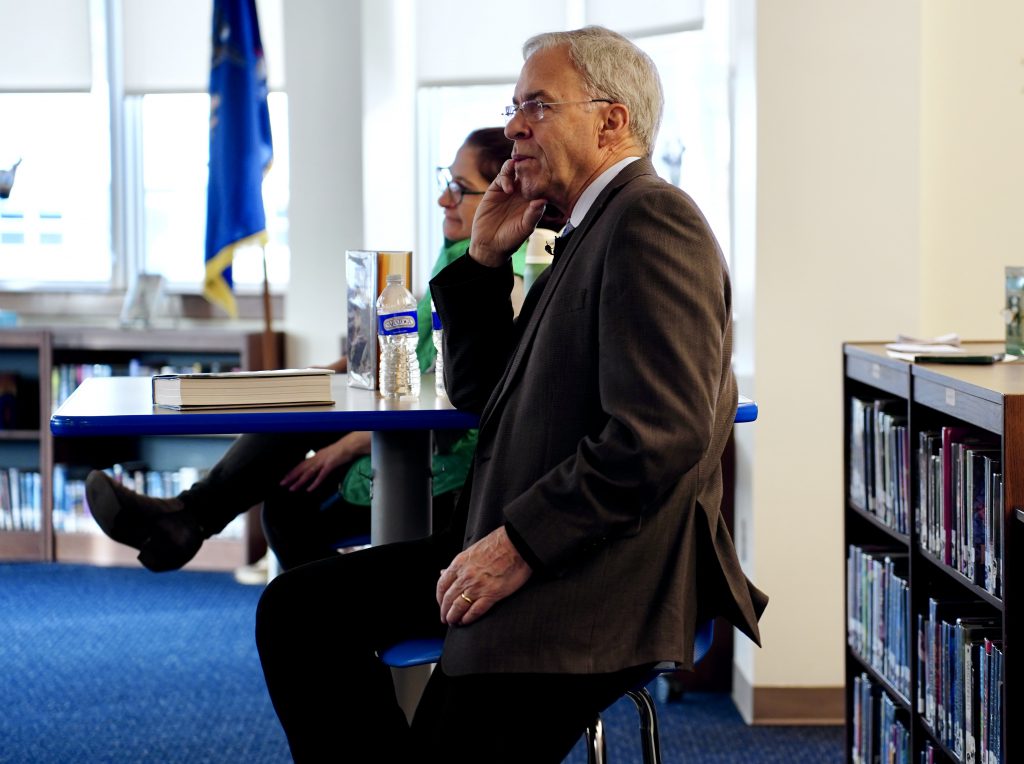 Author Rick Atkinson sitting, watching students, he has his arm on a table and his hand on his chin