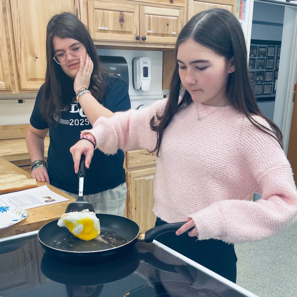 female student cooking an egg on a stovetop