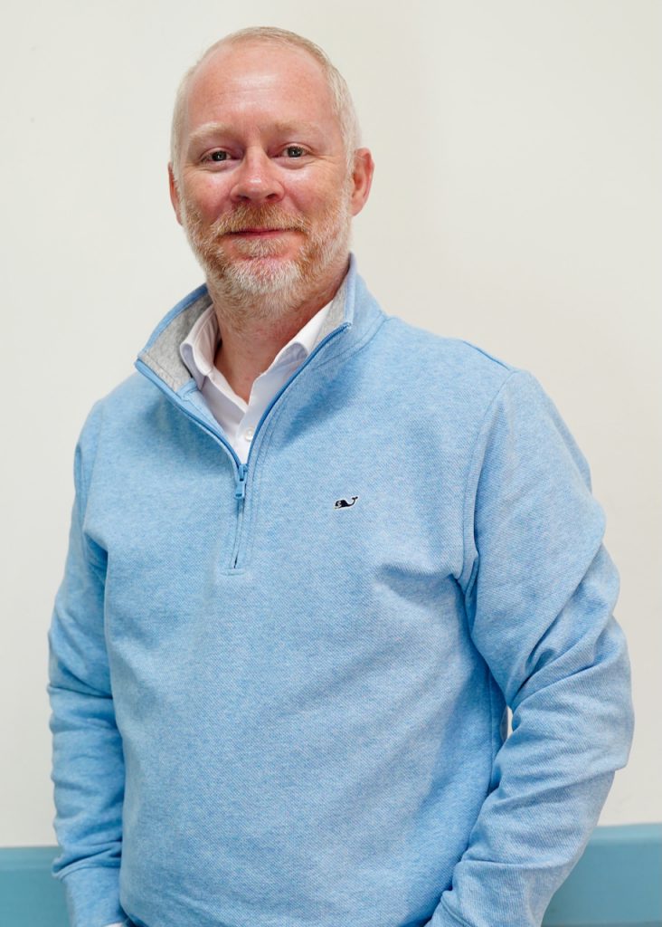 Man in blue sweater standing against a white wall