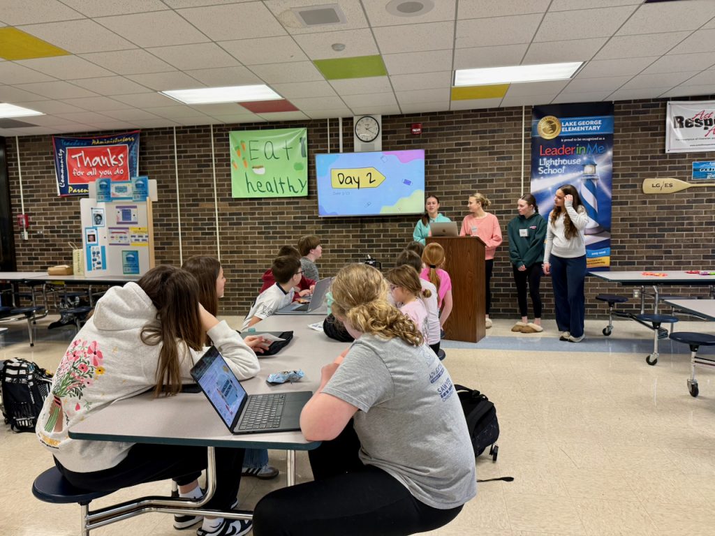 students at long tables looking towards a television