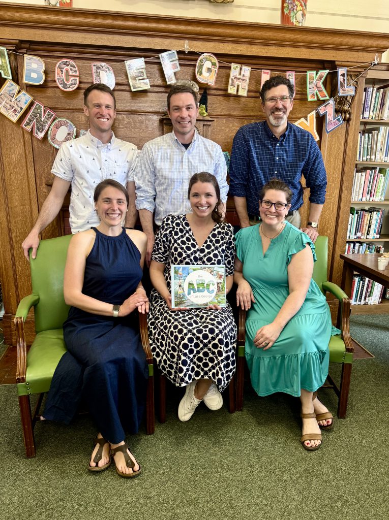 Six adults standing and sitting in front of alphabetical letters behind them in a library