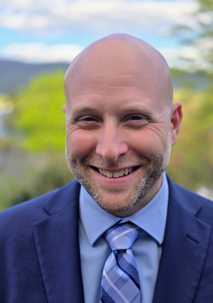 man in a blue suit and blue tie smiling at camera