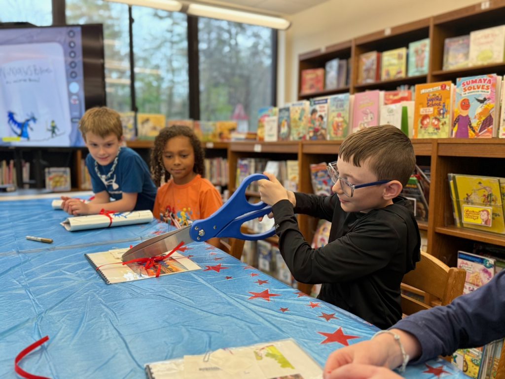 student cutting red ribbon with giant scissors