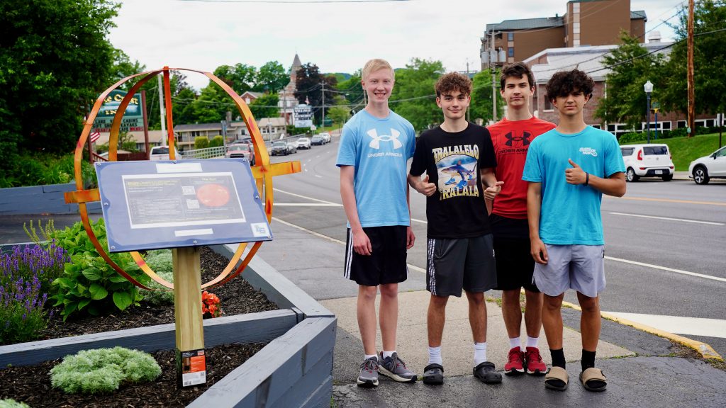 four students standing in front of a metal sun