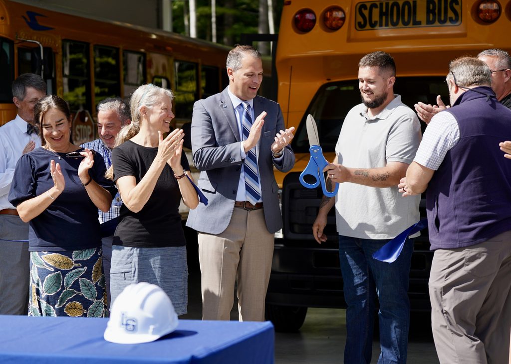 adults standing cutting a blue ribbon with large scissors