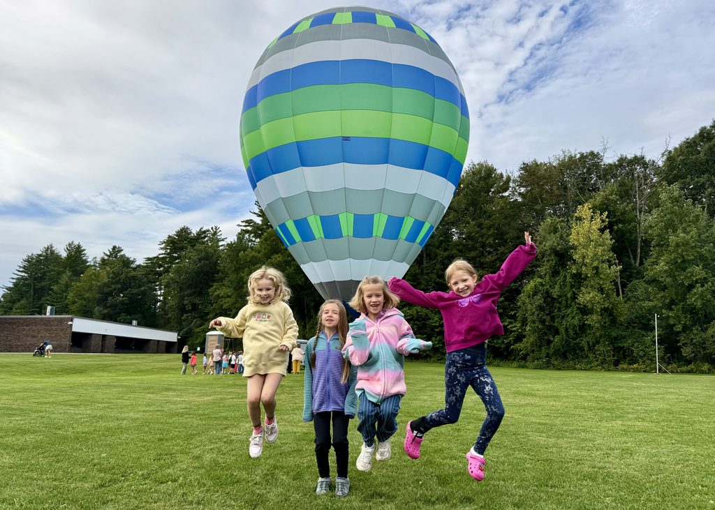 Four students jumping in front of a blue and green hot air balloon