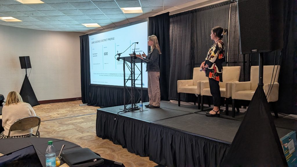 Two women presenting on a stage with a screen behind them