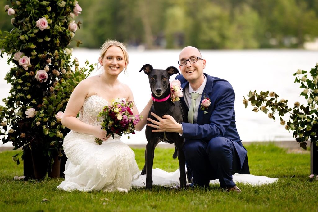 Two people in wedding clothes with a black dog in the middle