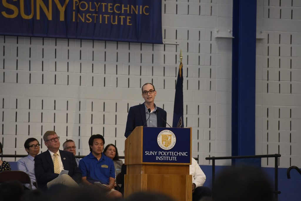 man speaking at a podium with people in the background